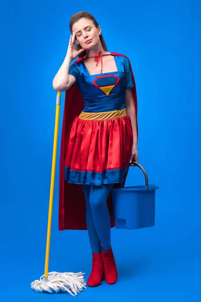 Mulher cansada em traje de super-herói com esfregona e balde para limpeza isolada em azul — Fotografia de Stock