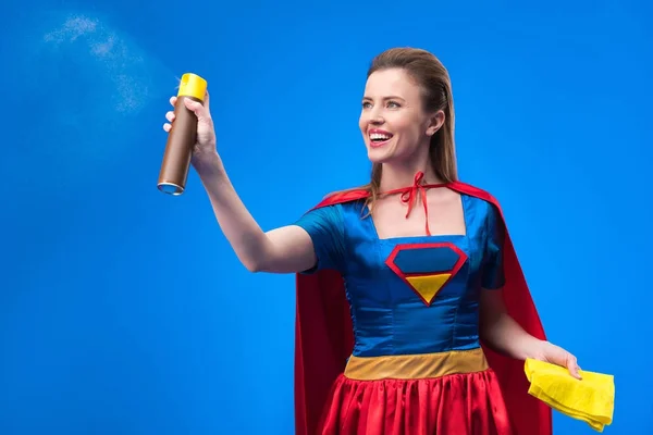 Retrato de bela super-mulher sorridente com pano e detergente para limpeza isolado em azul — Fotografia de Stock