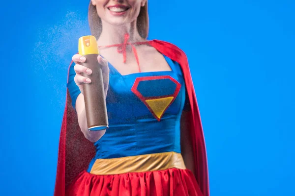 Vista parcial de supermujer sonriente con detergente en mano aislado en azul - foto de stock