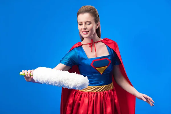 Portrait de femme souriante en costume de super héros avec brosse à poussière isolée sur bleu — Photo de stock