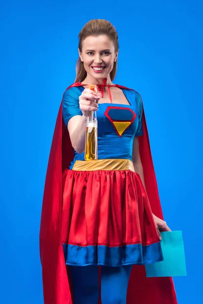 Mujer sonriente en traje de superhéroe con trapo y detergente en manos aisladas en azul - foto de stock