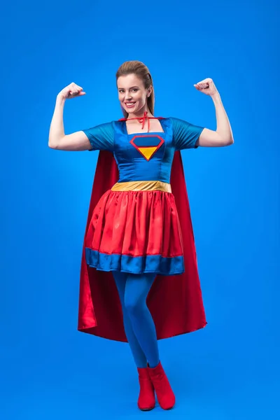 Sonriente mujer en traje de superhéroe mostrando músculos aislados en azul - foto de stock