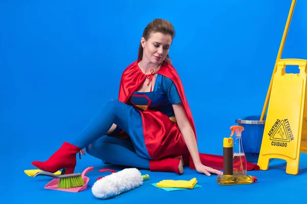 Femme en costume de super héros avec des fournitures de nettoyage autour isolé sur bleu — Photo de stock