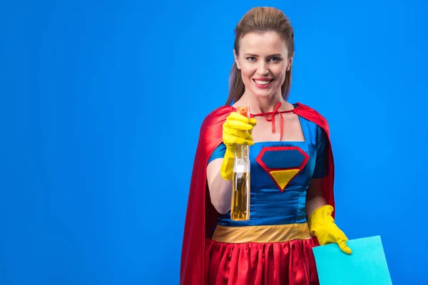 Retrato de mulher em traje de super-herói e luvas de borracha com pano e detergente isolado em azul — Fotografia de Stock