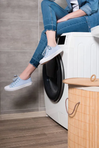 Vista parcial de ama de casa sentada en la lavadora en casa - foto de stock