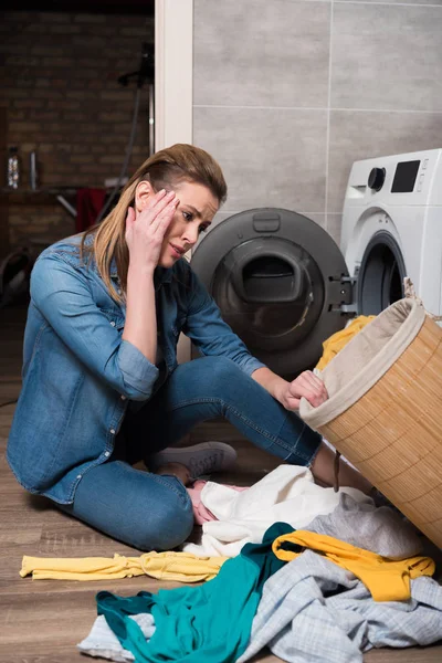 Femme au foyer émotionnelle regardant les vêtements avant de les mettre dans la machine à laver à la maison — Photo de stock