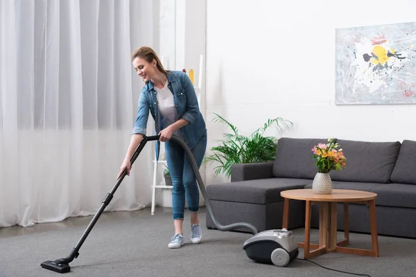 Atractiva mujer con aspiradora sala de limpieza en casa - foto de stock