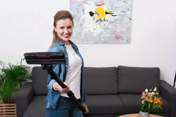 Portrait of cheerful woman holding vacuum cleaner in hands at home — Stock Photo