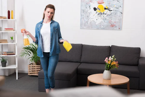 Femme fatiguée avec des fournitures de nettoyage dans les mains debout dans la chambre à la maison — Photo de stock