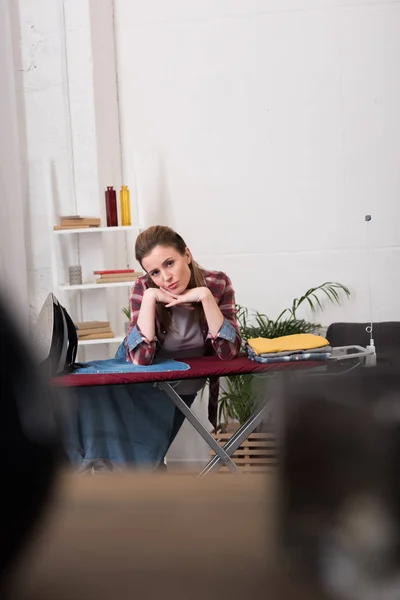 Portrait de femme fatiguée penchée sur planche à repasser à la maison — Photo de stock