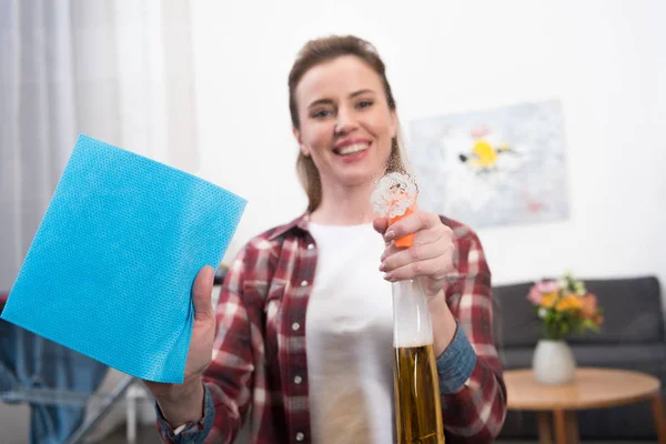 Foco seletivo da mulher sorridente com detergente e pano de limpeza em casa — Fotografia de Stock