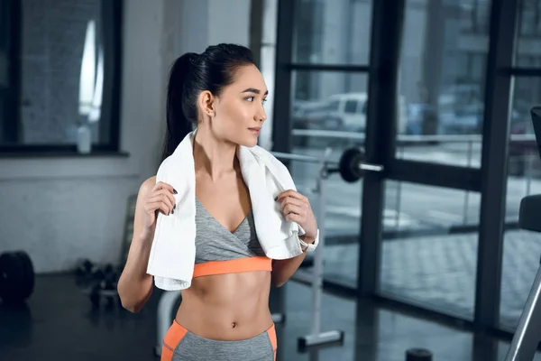 Young athletic woman with towel on shoulders at gym looking away — Stock Photo