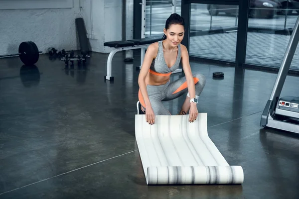 Привлекательная молодая женщина прокатка коврик йоги после упражнений в тренажерном зале — стоковое фото