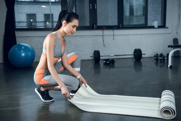Joven atlética mujer rodando estera de yoga después de ejercicios en el gimnasio - foto de stock