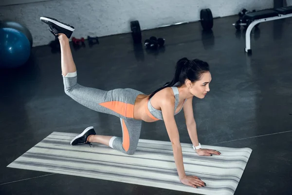 Jovem mulher exercitando no tapete de ioga no ginásio — Fotografia de Stock