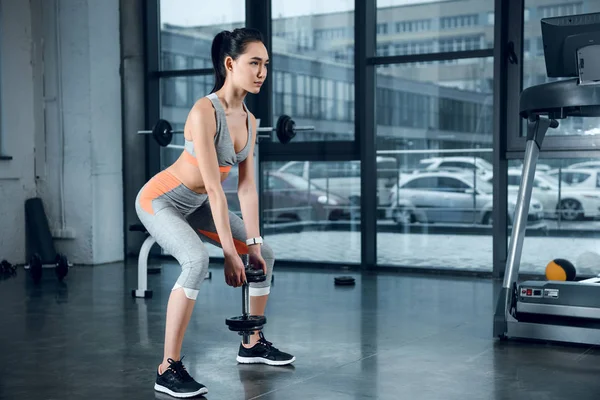 Giovane donna sportiva che fa squat con piatti di peso in palestra — Foto stock