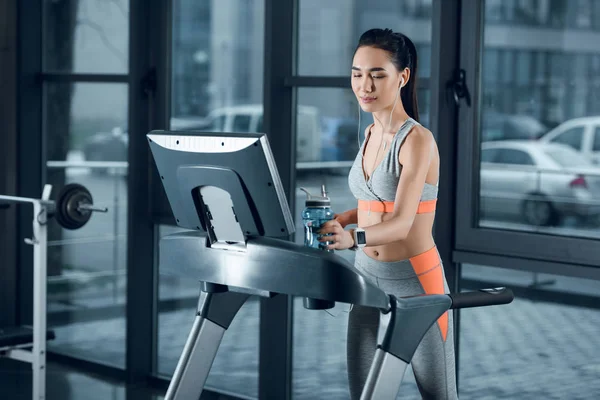 Young fit sportswoman jogging on treadmill at gym — Stock Photo