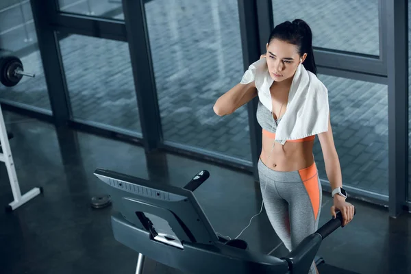 Vue grand angle de la jeune sportive athlétique essuyant avec une serviette après le jogging sur tapis roulant à la salle de gym — Photo de stock