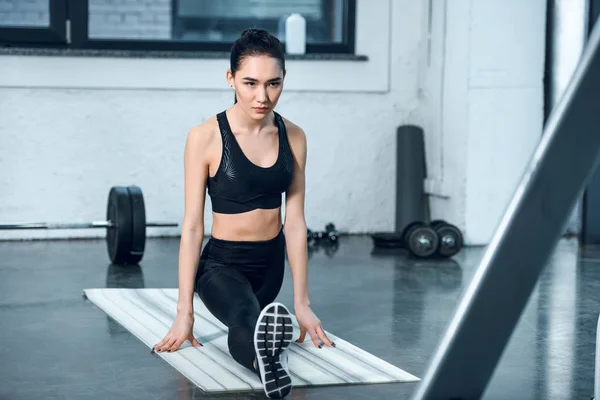 Young athletic woman stretching leg on yoga mat at gym — Stock Photo