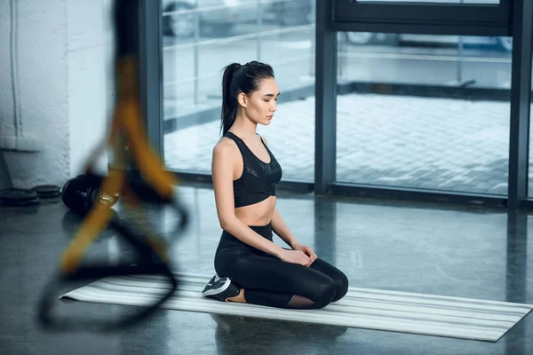 Atractiva joven mujer maditating en yoga mat en gimnasio - foto de stock