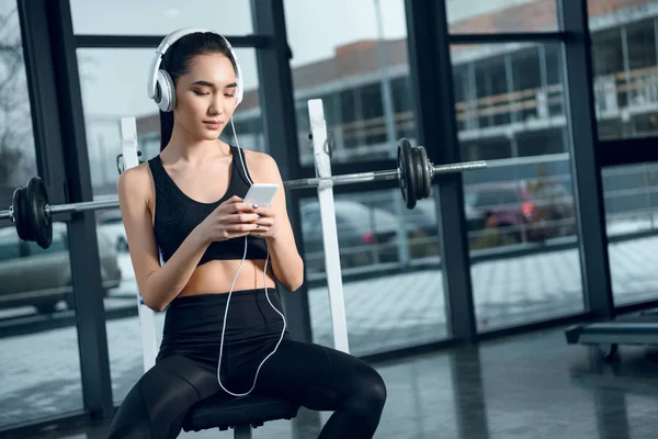 Junge, fitte Frau entspannt sich im Fitnessstudio und hört Musik mit Kopfhörern — Stockfoto