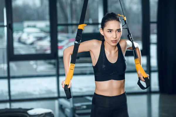 Belle jeune femme sportive travaillant avec des bretelles de suspension à la salle de gym — Photo de stock