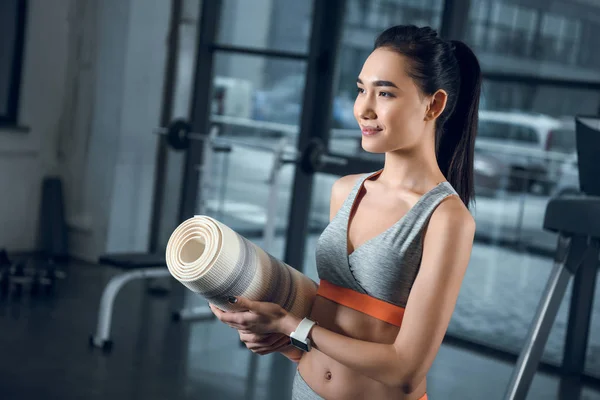 Giovane donna sportiva con rotolato stuoia di yoga in palestra — Foto stock