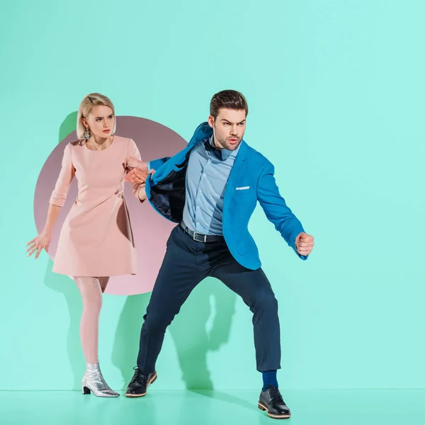 Angry boyfriend going with fashionable girlfriend through aperture on turquoise — Stock Photo