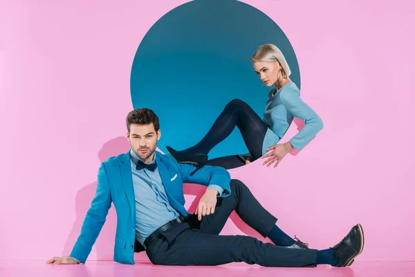 Attractive stylish couple sitting and looking at camera on pink — Stock Photo