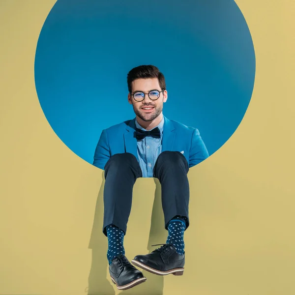 Sorrindo homem bonito em roupas da moda sentado em volta da abertura bege — Fotografia de Stock