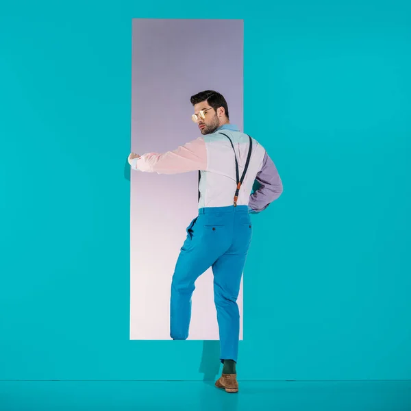 Rear view of handsome man in fashionable clothes going through frame on turquoise — Stock Photo