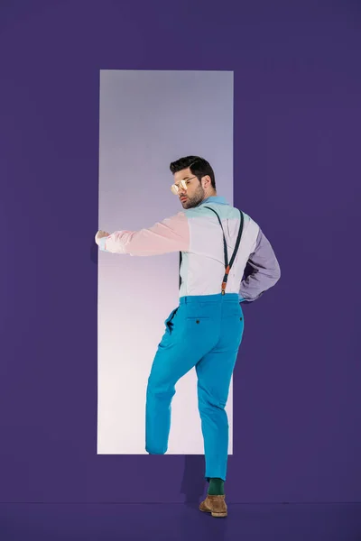 Rear view of handsome man in fashionable clothes going through frame on purple — Stock Photo