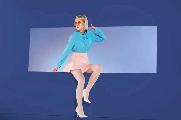 Привлекательная девушка в модной одежде сидит на отверстии изолированы на синий — стоковое фото