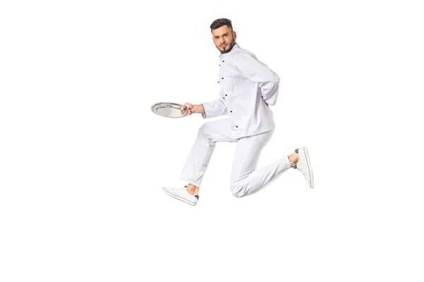 Young male chef holding plate while jumping and looking at camera isolated on white — Stock Photo