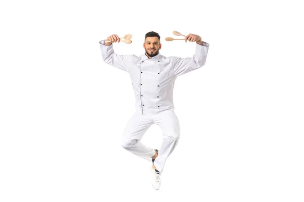 Joven chef masculino sosteniendo utensilios y sonriendo a la cámara aislado en blanco - foto de stock