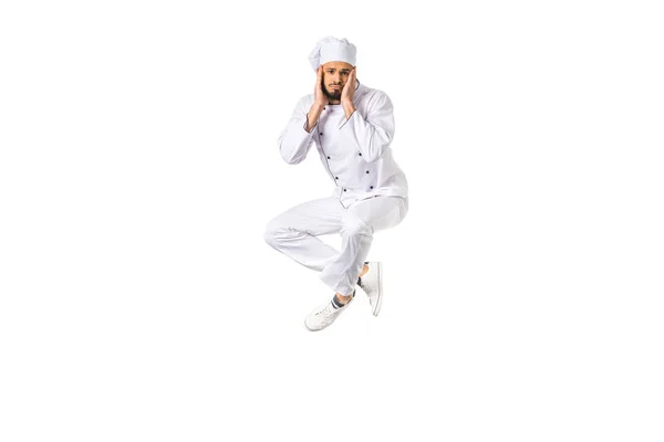 Upset young male chef jumping and looking at camera isolated on white — Stock Photo