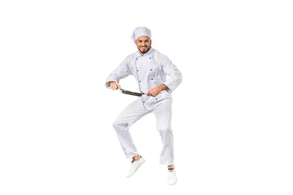 Happy young chef holding frying pan while jumping and smiling at camera isolated on white — Stock Photo