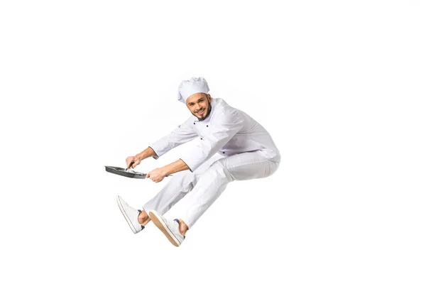 Feliz joven chef con la sartén saltando y mirando a la cámara aislada en blanco - foto de stock