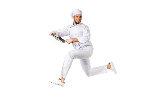 Sonriente chef con sartén saltando y mirando a la cámara aislada en blanco - foto de stock