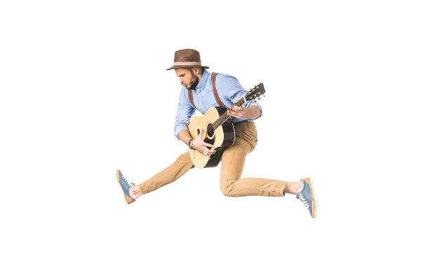 Schöner junger Musiker mit Hut, der Gitarre spielt, während er isoliert auf Weiß springt — Stockfoto