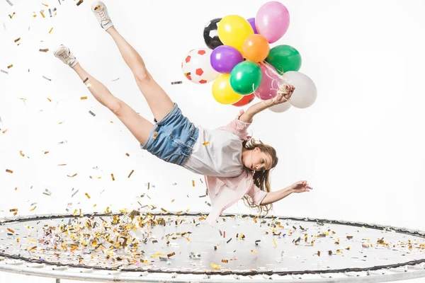 Дівчина тримає різнокольорові кульки і падає на батут ізольовано на білому — стокове фото