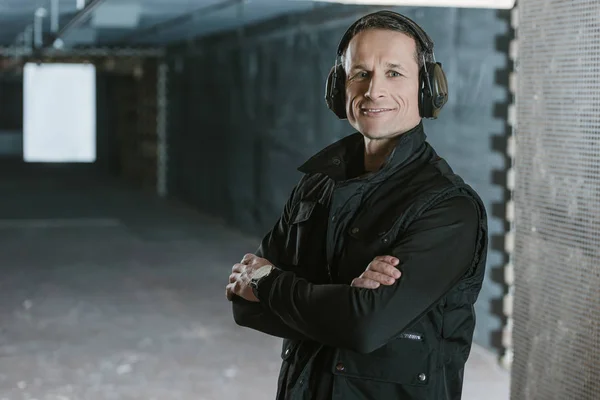 Smiling handsome man with crossed arms looking at camera in shooting range — Stock Photo