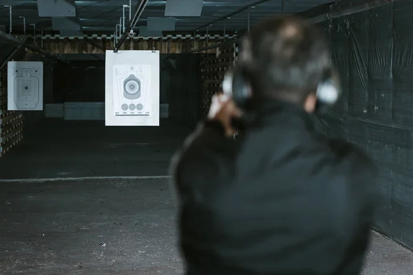 Rear view of man aiming gun at target in shooting range — Stock Photo