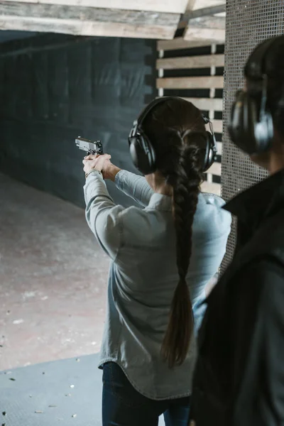 Rear view of girl shooting with gun in shooting range — Stock Photo