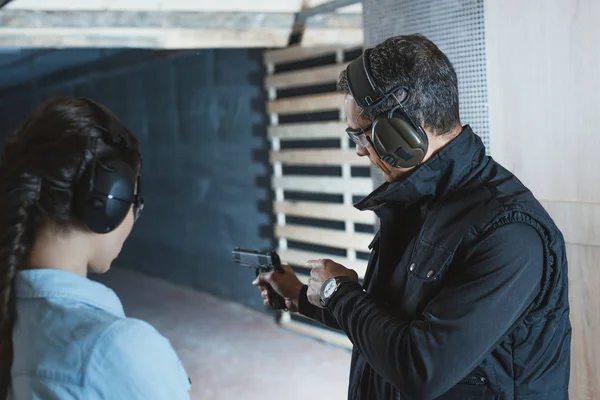 Visão traseira do instrutor masculino que descreve a pistola ao cliente fêmea na galeria de tiro — Fotografia de Stock