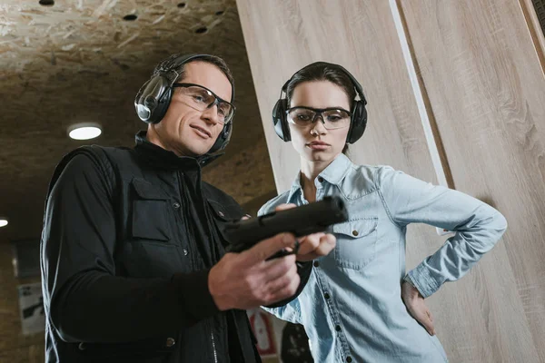 Instrutor masculino descrevendo pistola para cliente feminino na galeria de tiro — Fotografia de Stock