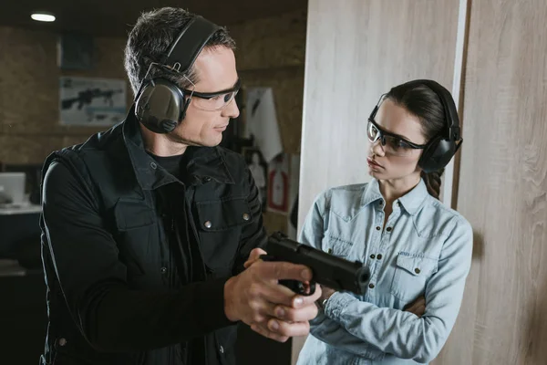 Instructor masculino describiendo arma a cliente femenino en galería de tiro - foto de stock