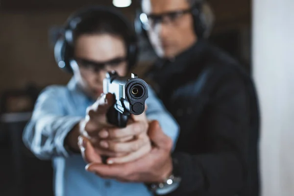 Instructor helping customer in shooting gallery with gun on foreground — Stock Photo