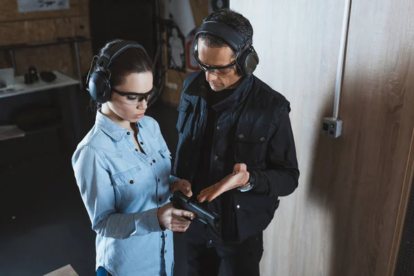 Male instructor describing gun to female customer in shooting range — Stock Photo