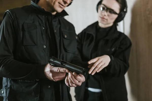 Cropped image of instructor showing gun to female client in shooting gallery — Stock Photo